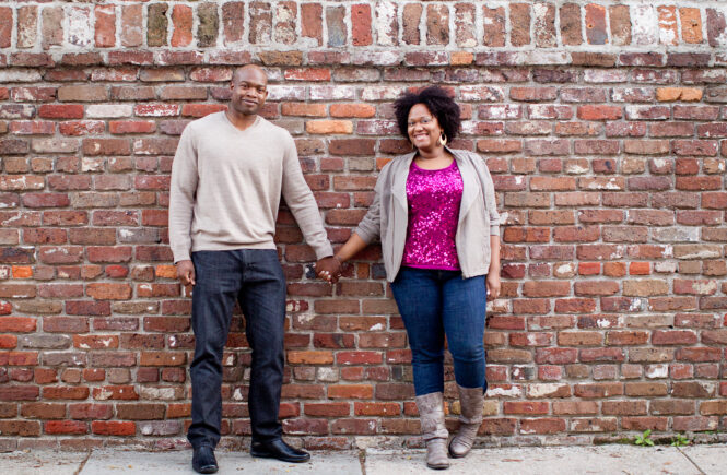 Lennie and Monica holding hands in front of a brick wall.